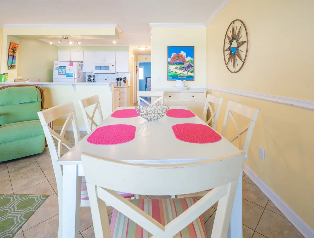 An inviting interior dining area with a table dressed in pink placemats, a green accent chair, and vibrant wall art. The space feels cozy and is clearly designed for group meals, gatherings, or board game nights.