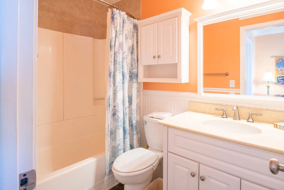 A bright, clean bathroom with a bathtub, shower curtain, vanity, and large mirror, evoking a sense of freshness and relaxation—ideal for unwinding after a day at the beach or preparing for a new adventure.